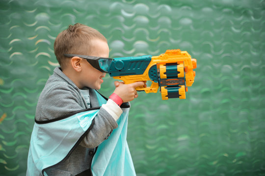 Small preschooler boy with blaster prepare for attack and play with friends in protective glasses. Excited Child with darts toy gun on the play field