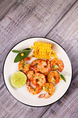 Grilled shrimps and corn garnished with lime and sage leaves. Prawns on white plate. View from above, top studio shot