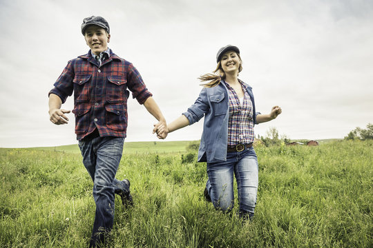 Couple holding hands running through field, looking at camera smiling