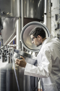 Side view of brewer in brewery wearing lab quality checking beer