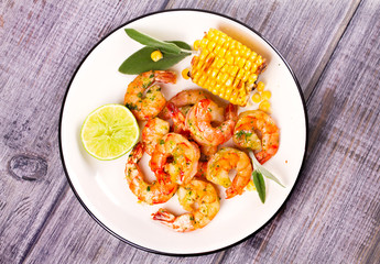Grilled shrimps and corn garnished with lime and sage leaves. Prawns on white plate. View from above, top studio shot