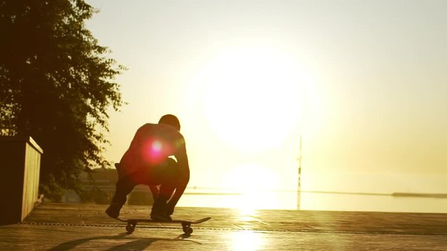 Silhouette of young Caucasian male riding skateboard and doing kickflip trick. Footage with sea on background and beautiful sunset