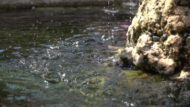 falling water drops hits and explodes on a stone water fountain liquid crash in slow motion