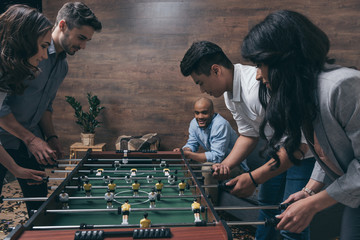 Smiling young friends playing table football together indoors