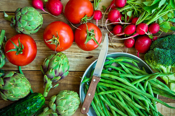 Variety of fresh colorful organic vegetables green beans, tomatoes, red radish, artichokes, cucumbers on wood kitchen table, copy space, top view, healthy food, vegetarian, vegan