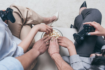 cropped shot of young friends eating popcorn while playing video games at home