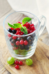 Fresh berries of black and red currant, gooseberry in a transparent glass mug on a wooden surface. Summer harvest of berries