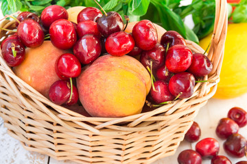 Ripe fresh organic peaches, sweet cherries in a fruit wicker basket on wood garden table, herbs, melon, summer, outdoors, harvest, healthy diet, clean eating, vegan, vegetarian