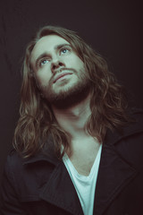 Portrait of handsome stylish bearded young man with long hair looking up