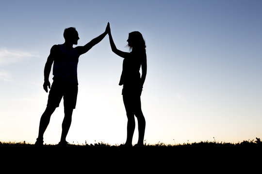 Happy silhouette couple holding up hands against the sky at dusk