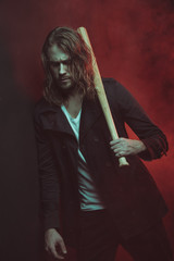 Serious long haired man holding baseball bat on shoulder and looking down