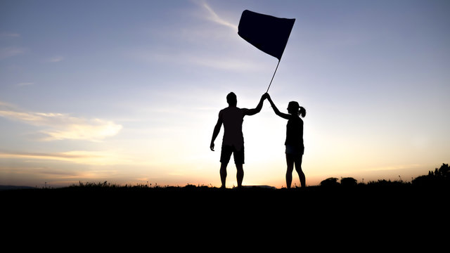 silhouette of two people at with sunset on the back with flag