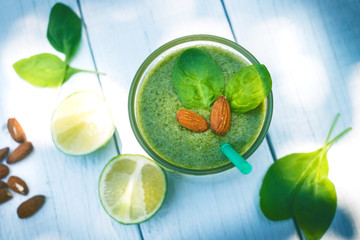 Spinach smoothie on a wooden white background. Glass of smoothie with  leaves of spinach, nuts, limes. Healthy food. Breakfast. Natural light. 