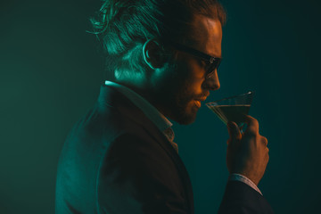 profile of young caucasian man in suit drinking cocktail from glass