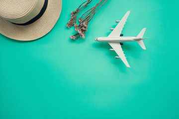 Flat lay design of travel concept with plane, straw hat on green background with copy space.