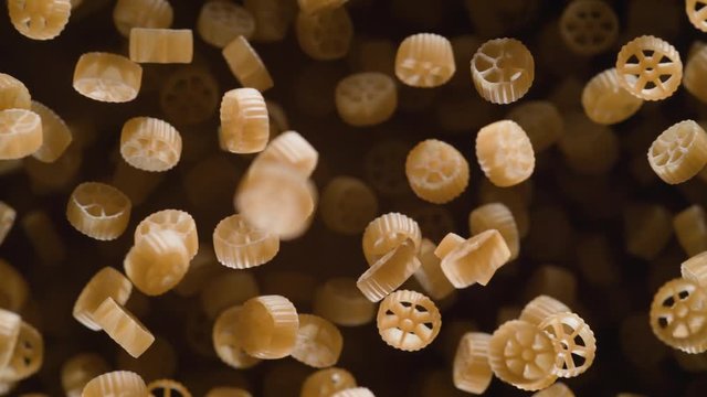 Raw wagon wheels pasta flies after being exploded against black background. Shot with high speed camera, phantom flex 4K. Slow Motion.