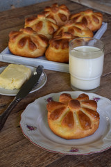 Buttermilk dinner buns in flower form served with butter, knife, glass of milk on wooden background. Fresh baked brioche. Homemade baking.