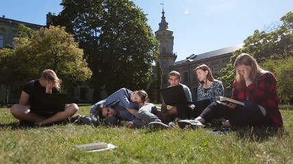 Group of tired students studying hard on park lawn - Powered by Adobe