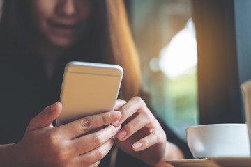 A beautiful Asian woman with smiley face holding and using smart phone with coffee cup on wooden table in the cafe