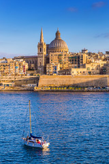 Valletta, Malta - St.Paul's Cathedral in golden hour at Malta's capital city Valletta with sailboat and beautiful blue sky