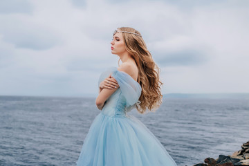 Fototapeta na wymiar Beautiful young girl in a long blue lush dress is standing on the beach