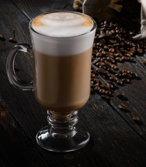 Irish coffee with cappuccino foam on dark wooden background with coffee beans