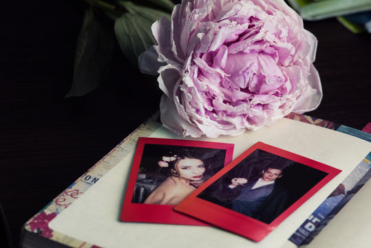 Snapshots of a young couple lying on a vintage diary. Pink wilted blurred peony on the background. Fading memories concept. Nostalgia and love.