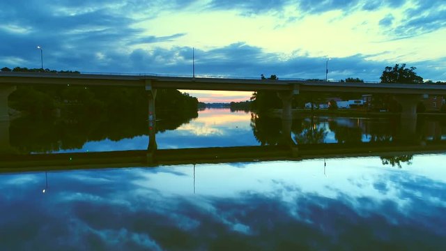 Flying under scenic bridge with smooth waters reflecting twilight sky.
