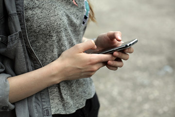 Young woman using smart phone on the street; people, technology and addiction concept.
