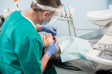 Male dentist with dental tools - mirror and probe checking up patient teeth at dental clinic office. Medicine, dentistry and health care concept. Dental equipment