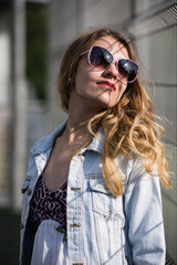 Stunning female model wearing stylish denim jacket, trendy sunglasses, and colored vibrant dress. Urban fashion blogger posing with a trendy 2017 summer look.