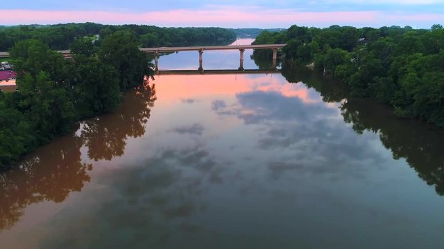 Flying over scenic bridge, smooth waters reflecting moody twilight sky.
