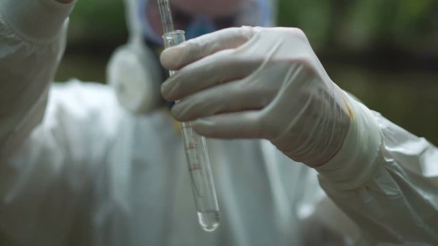 Anonymous ecologist in protective suit holding glass test tube.