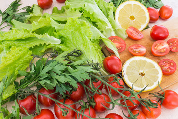 Cherry tomatoes, lemon plastics, parsley and lettuce leaves covered with drops of water lie on the kitchen table