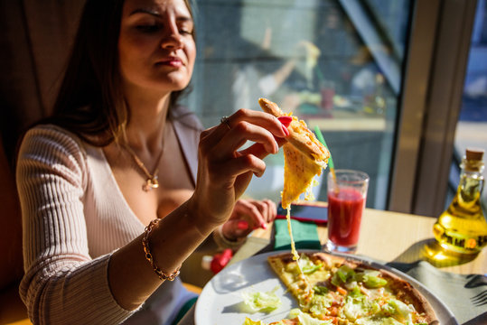 Beautiful young woman eating pizza in the restaurant. Happy and joyful lifestyle. Healthy and junk food concept.