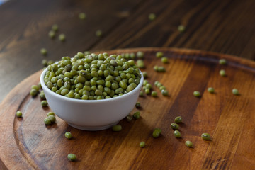 Organic mung beans on white ceramic bowl over wooden background.