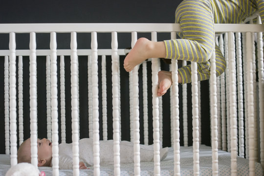 Girl climbing on crib and brother lying inside