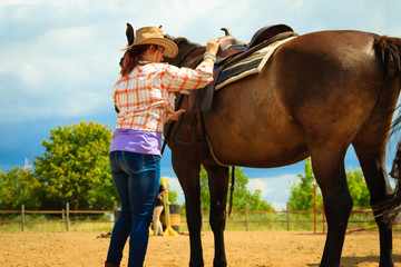 Cowgirl getting horse ready for ride on countryside