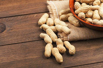 From above plate with whole peanuts on canvas bag. Wooden background.