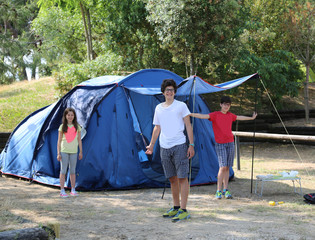 Three smiling children mount the tent in the campsite © ChiccoDodiFC