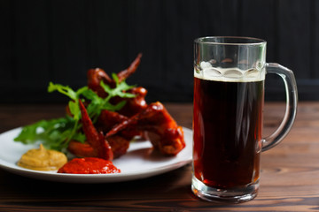  A mug of dark beer with crusty grilled chicken wings on wooden table