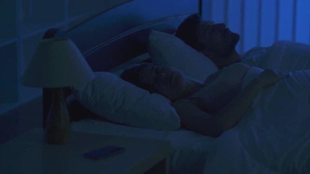 The woman phone on the bed near the man. night time