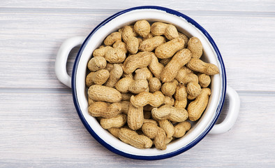 From above plate with whole peanuts on metal container, on wooden table.