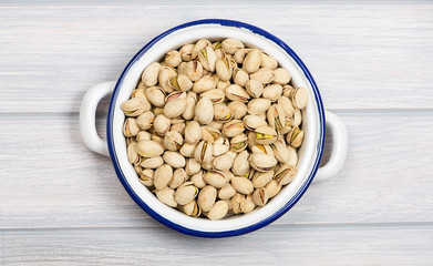 From above plate with pistachios on metal container, on wooden table.