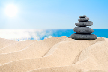 Fototapeta na wymiar On the Beach - balanced stones arranged on a sand dune in front of beautiful azure sea 