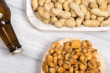 Cerveza with peanuts  and toasted corn on wooden background.