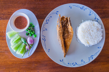 Thai food top view,fried fish with rice, shrimp paste, chilli sauce and vegetables on wooden table.