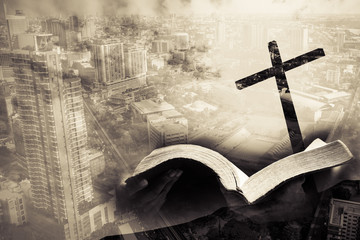 mixed media of cross and city and hand hold bible - obrazy, fototapety, plakaty