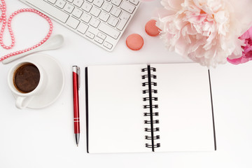 Office desk table with computer, cup of coffee and peony flowers. White wooden background.