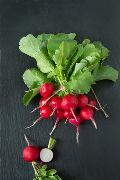 Ripe bunch red radish with foliage on a black slate dish as background. Top view.